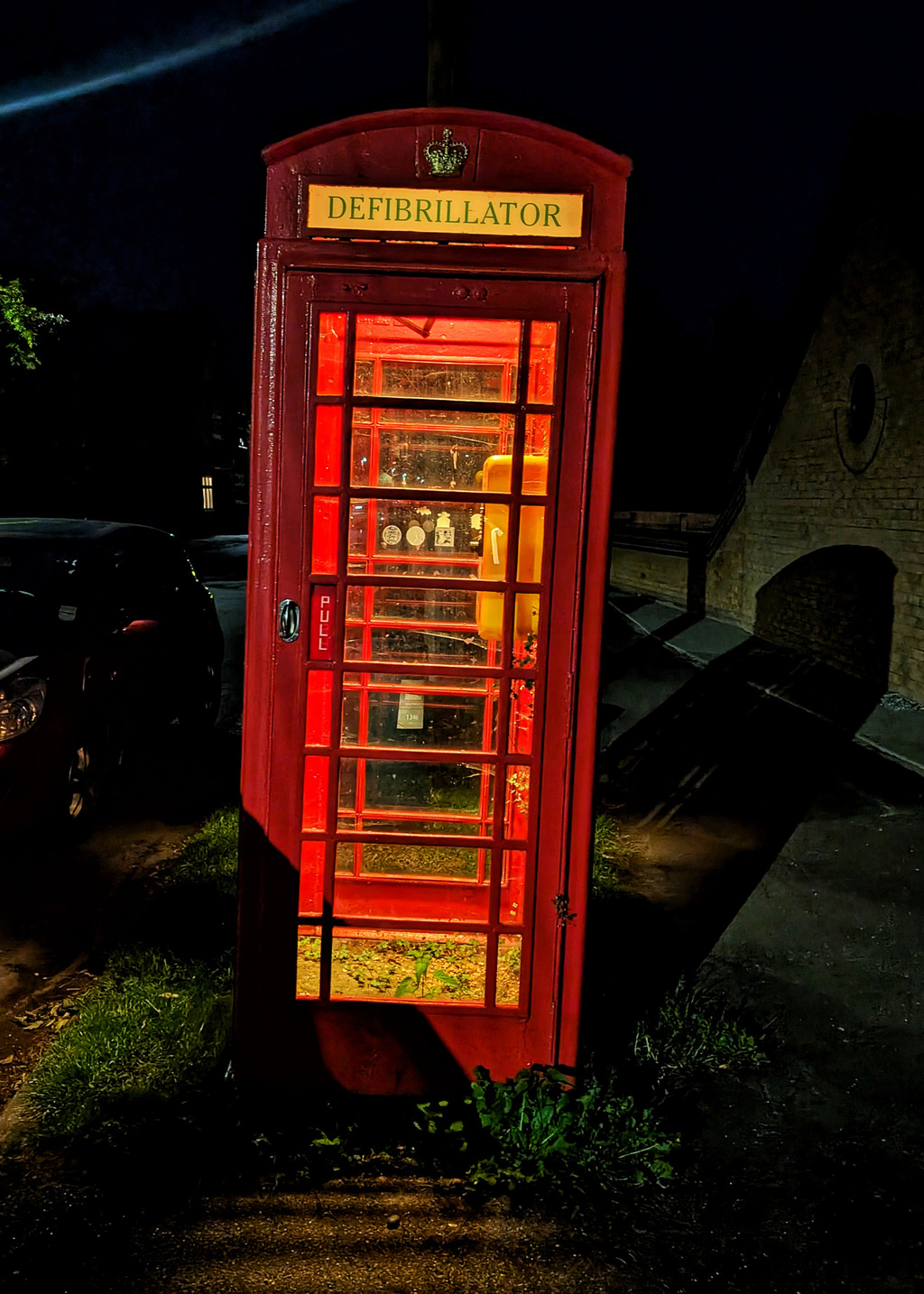 A phtograph of a red phone box lit up at night, now re -purposed as a defibrillator store.
